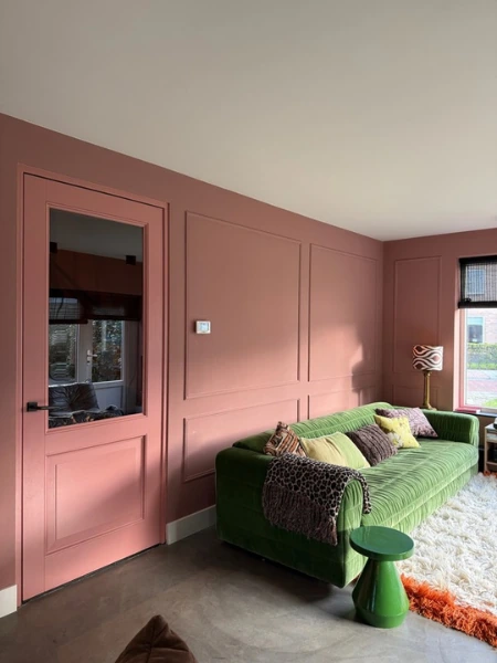 Roze wand met sierlijsten achter een groene bank