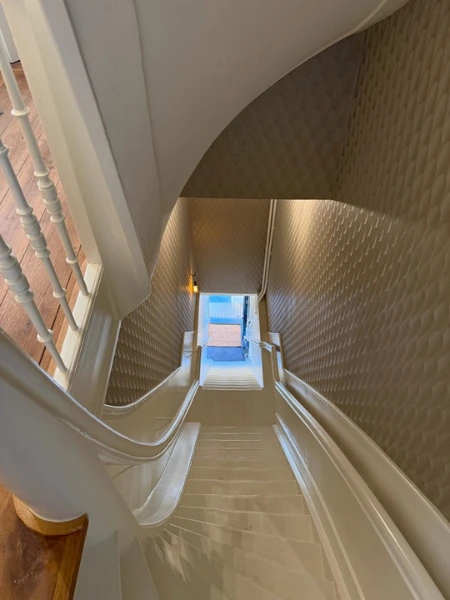 Trappenhuis met een gebogen wand met textuur en witte leuningen